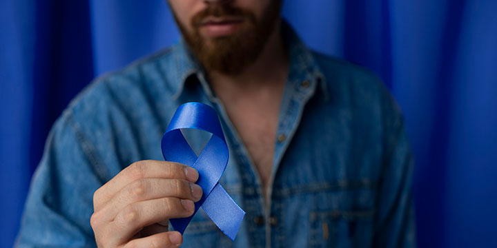 Hombre sosteniendo en su mano una cinta azul por el día del cáncer de próstata