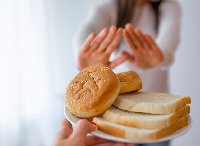 mujer rechazando con las manos un plato de pan - Enfermedad Celíaca
